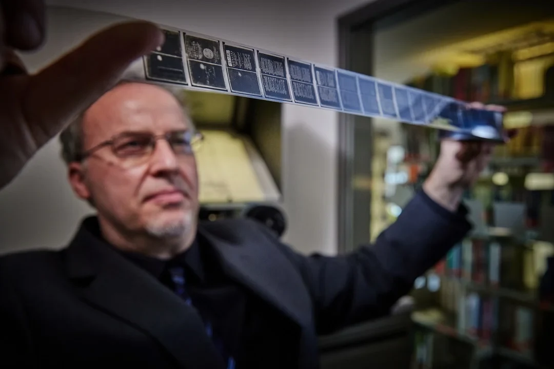 Eine Wissenschaftlerin und ein Wissenschaftler arbeiten hinter einer Glasfassade und mischen Chemikalien mit Großgeräten.